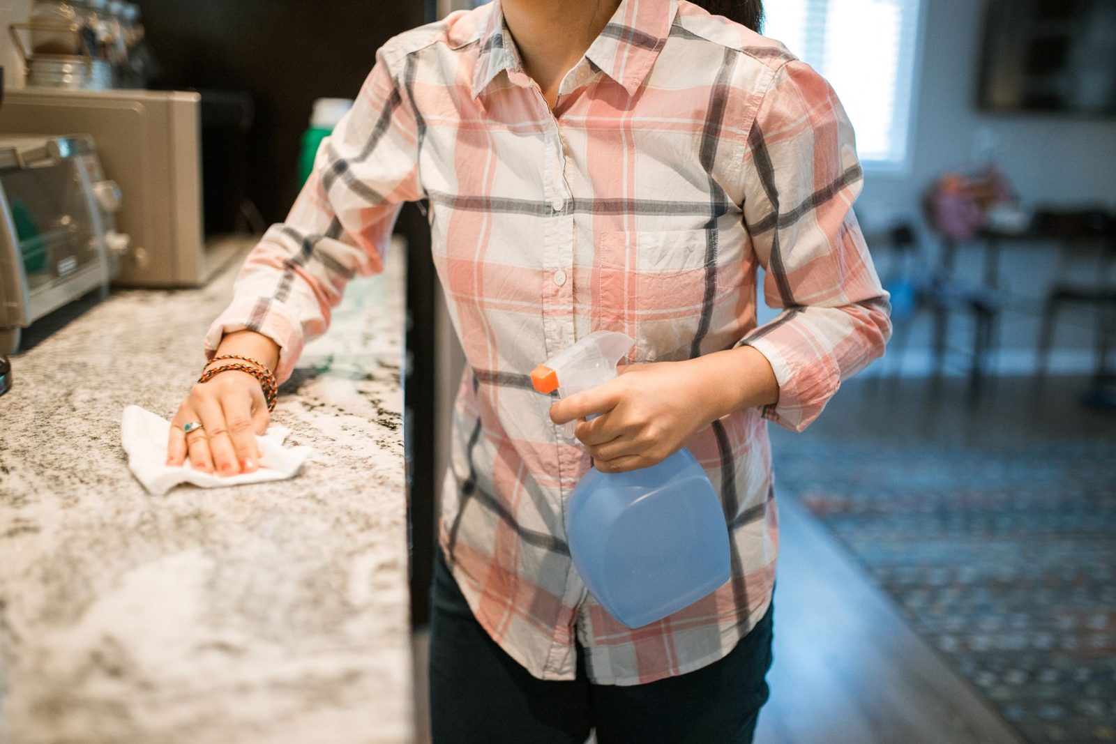 Cleaner wiping a kitchen counter with a spray bottle