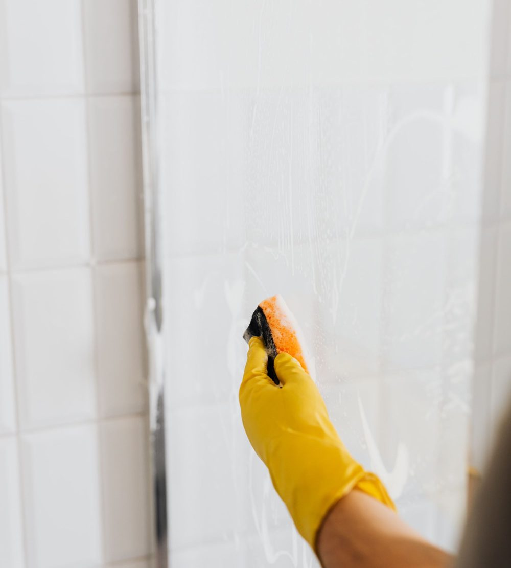 Cleaning a glass shower wall with a yellow glove