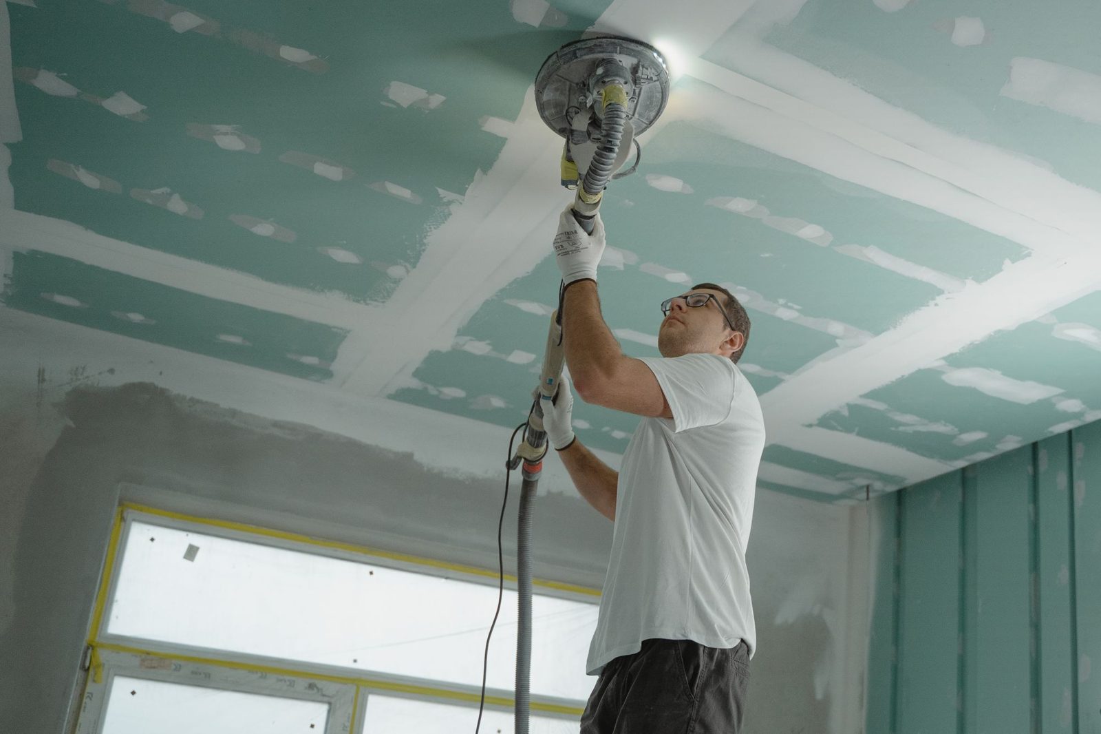 Contractor sanding a ceiling, creating dust before a post-construction clean